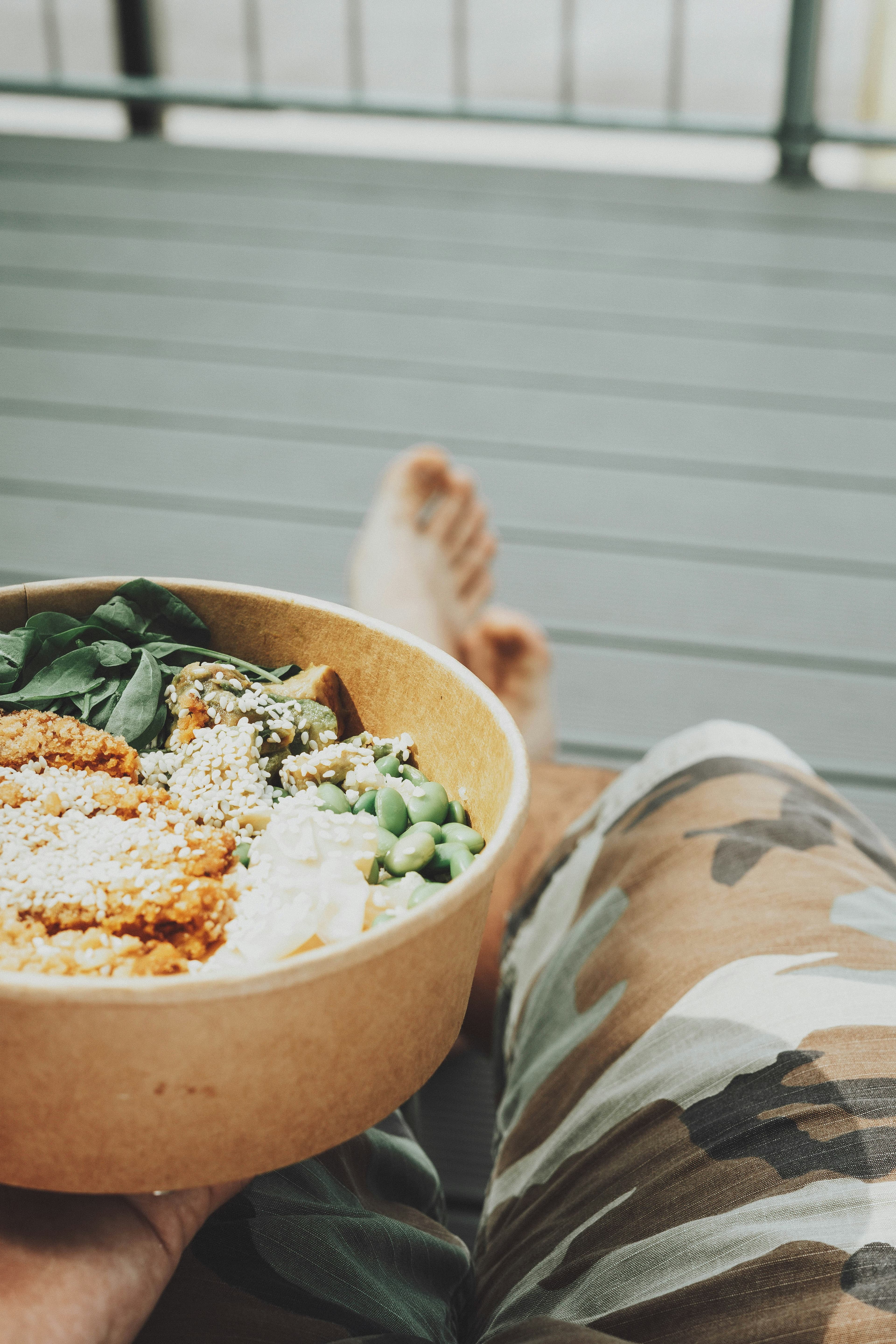 Person holding a healthy bowl of greens and grains outdoors