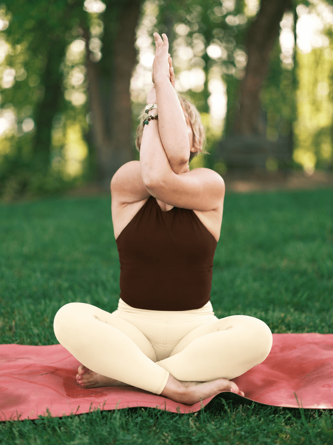 Woman practicing seated eagle pose outdoors on a yoga mat